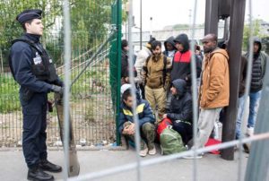Un groupe de migrants attend devant un policier pour entrer dans le centre humanitaire pour réfugiés du nord de Paris.
